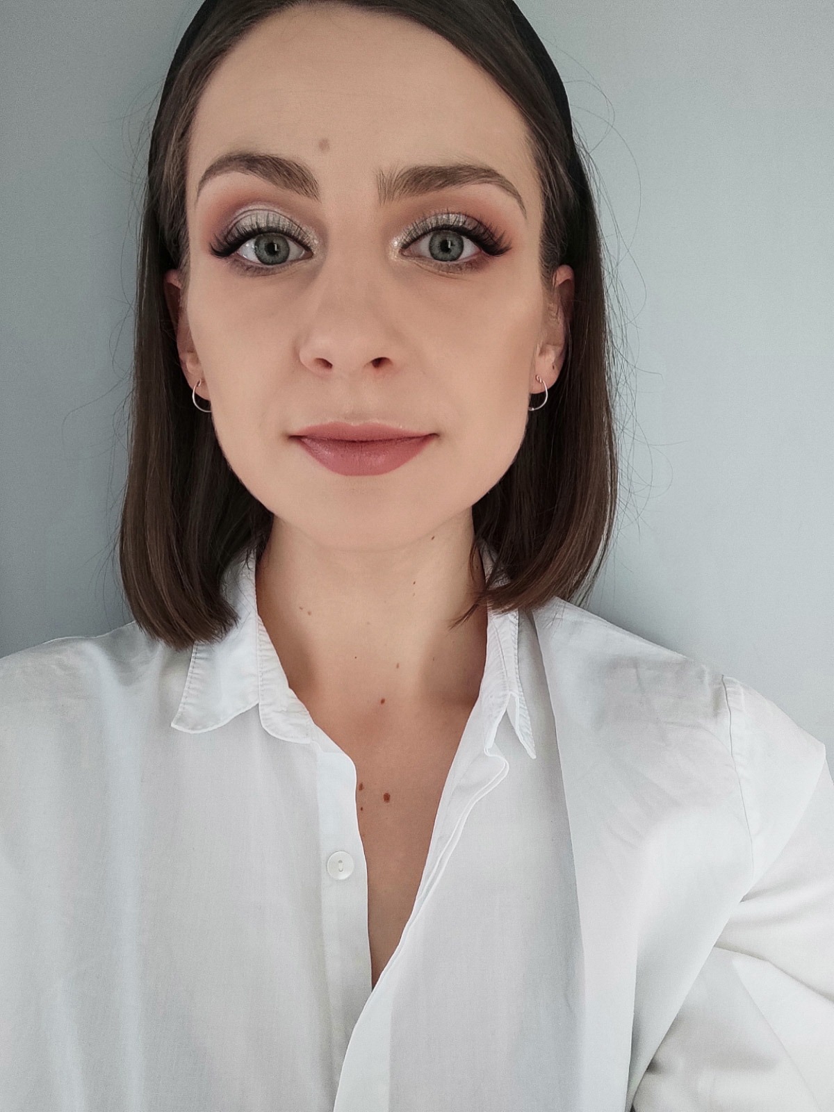 Portret kobiety z subtelnym makijażem oczu w odcieniach brązu i srebra, delikatnie podkreślone usta i krótka fryzura bob, ubrana w białą koszulę.