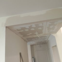 Piotr-Bud Piotr Kołodyński - Sufit w trakcie szpachlowania z widocznymi punktami po wkrętach, wystające przewody oświetleniowe, fragment ściany i drzwi w tle