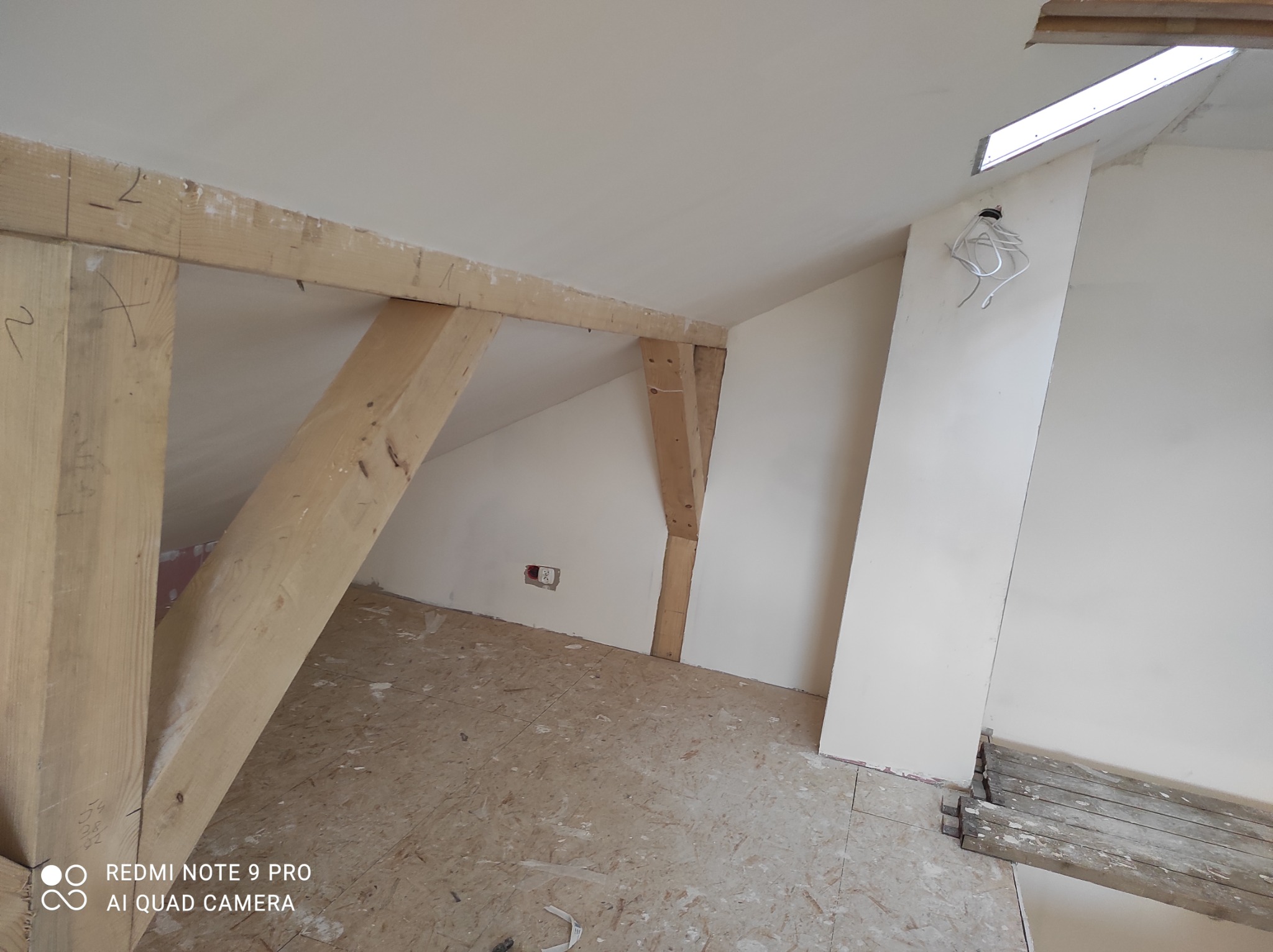 Adaptacja poddasza: drewniana konstrukcja nośna, szpachlowane ściany, przygotowane do malowania, widoczne kable elektryczne i fragment rusztowania.