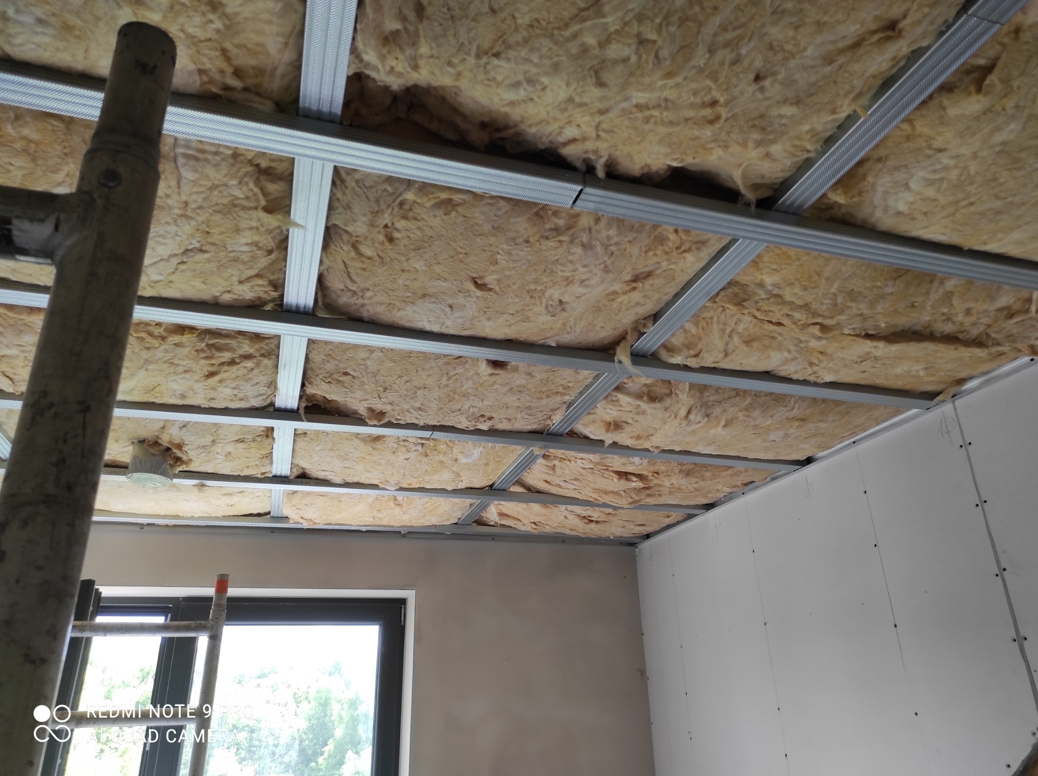 Montaż sufitu podwieszanego z wełny mineralnej w metalowej konstrukcji, widoczna drabina malarska i fragment ściany z płyt kartonowo-gipsowych.