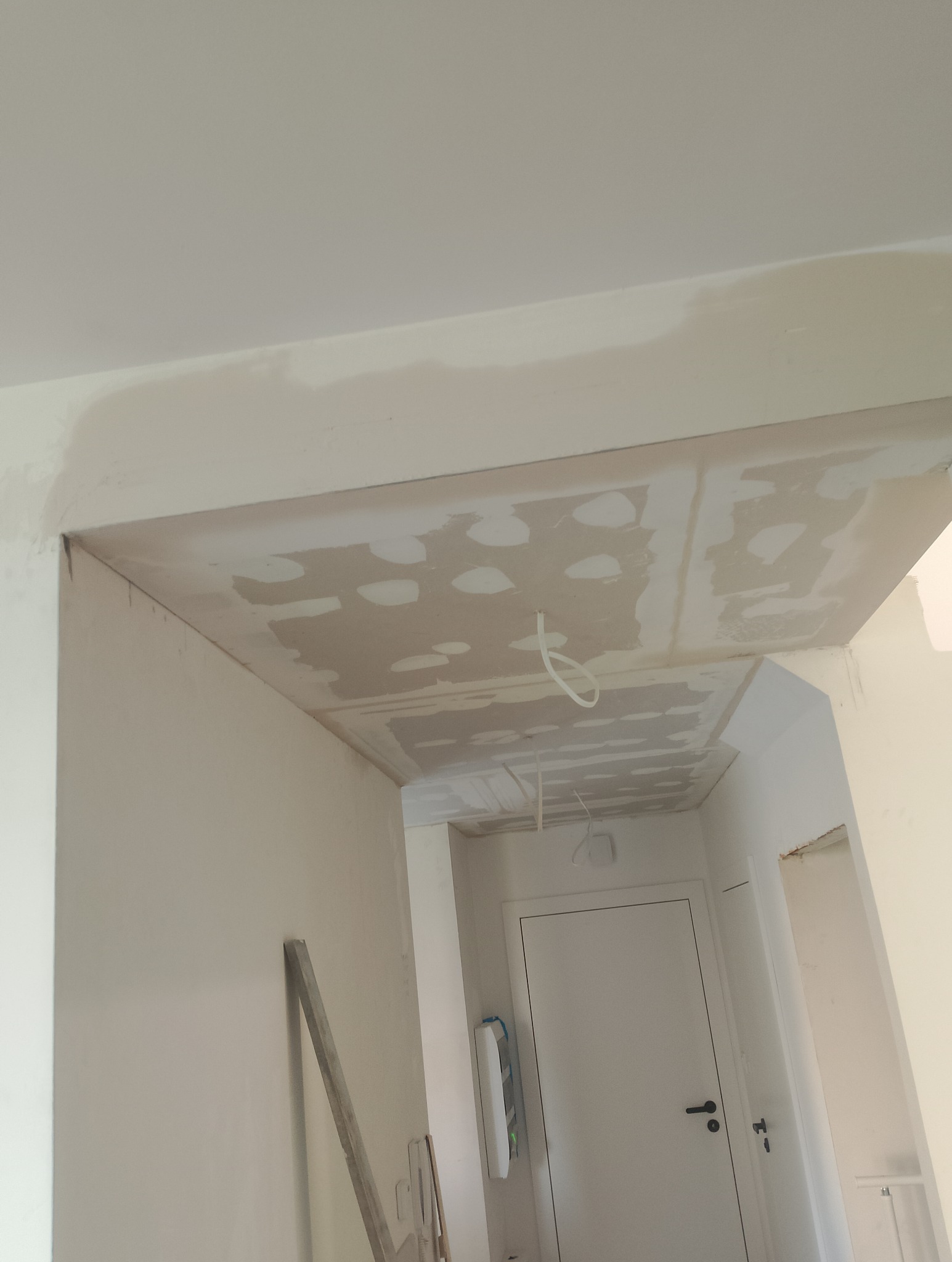 Sufit z płyt kartonowo-gipsowych w trakcie szpachlowania, widoczne łączenia płyt i instalacja elektryczna przed ostatecznym wykończeniem w korytarzu mieszkania.