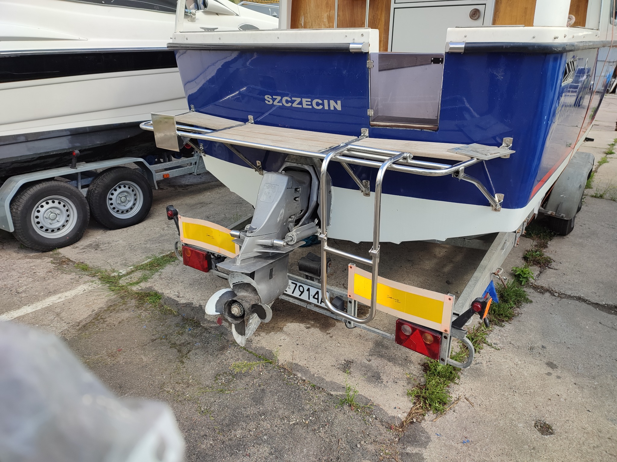 Zewnętrzny silnik łodzi z drabinką i platformą z drewna, umieszczony na przyczepie, z napisem 'Szczecin' na burcie.