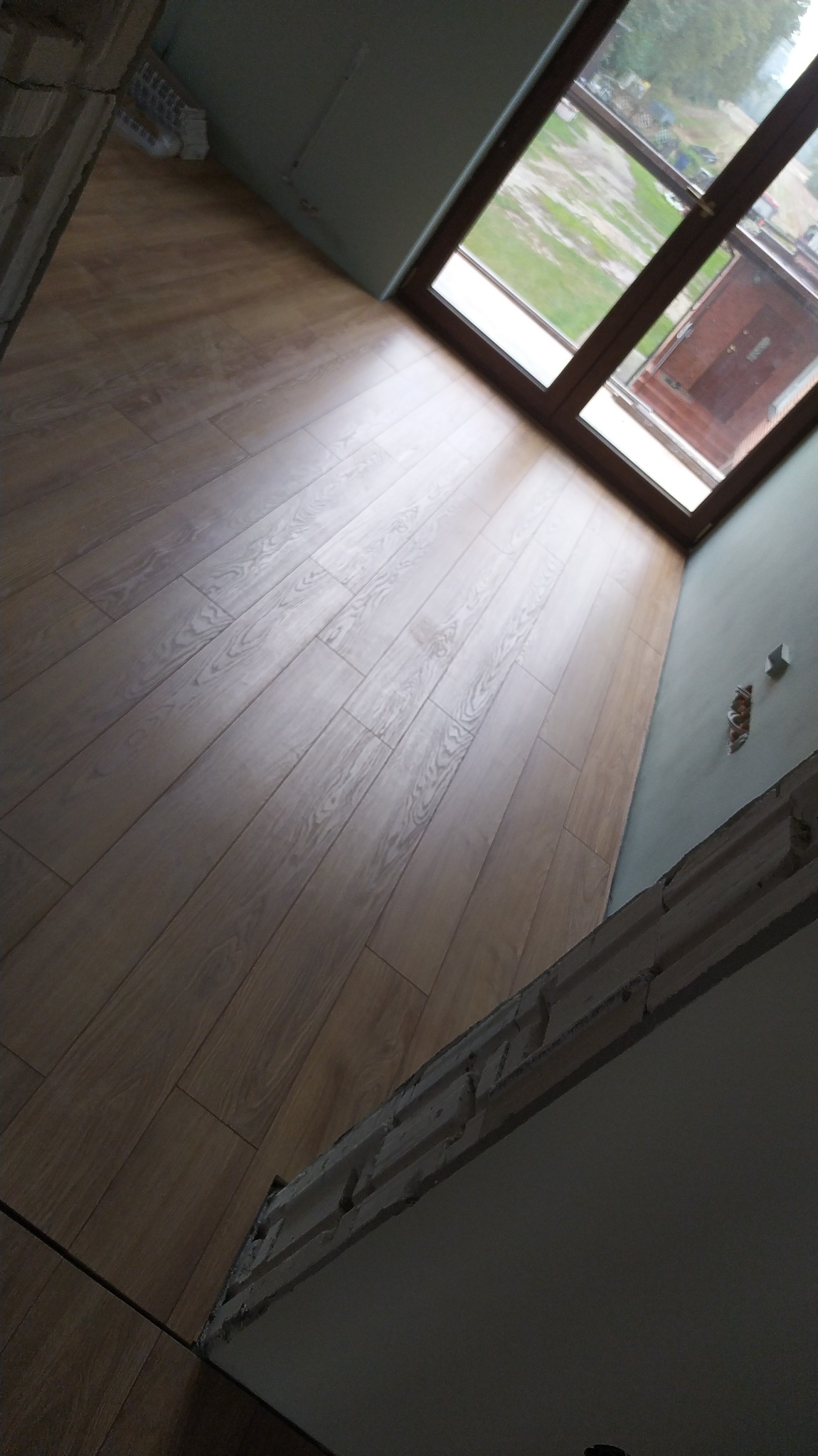 Ukończona podłoga z paneli w jasnym odcieniu drewna, widok z góry na nowo wykończone wnętrze z oknem.