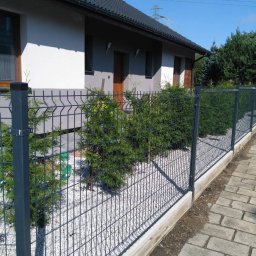 Hermes ogrodzenia - Nowoczesne ogrodzenie panelowe z metalu, z podmurówką betonową i białym grysem, oddzielające posesję z domem jednorodzinnym, z widoczną kostką brukową chodnika.