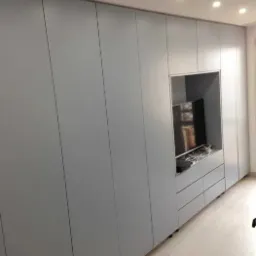 Szara zabudowa ścienna z szafami z wnęką na telewizor i szufladami, oświetlenie sufitowe punktowe.