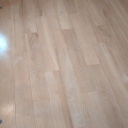 Usługi remontowo-wykończeniowe - Ułożona podłoga z paneli imitujących jasne drewno, widoczne nierówności przy ścianie.