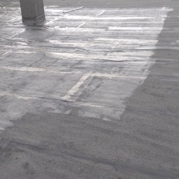 Usługi remontowo-wykończeniowe - Szare, płaskie pokrycie dachowe z papy bitumicznej, z widocznymi łączeniami i śladami napraw, częściowo pokryte jasną, refleksyjną powłoką ochronną.