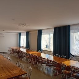 Usługi remontowo-wykończeniowe - Jasne wnętrze sali konferencyjnej z długimi drewnianymi stołami i metalowymi krzesłami, zasłony w kolorze ciemnego turkusu przy oknach.