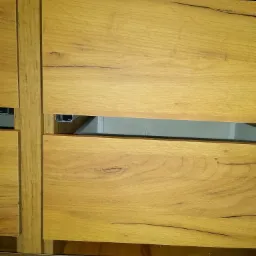 Szczegółowe ujęcie frontów szuflad z drewna o jasnym odcieniu, widoczna struktura słojów i delikatne pęknięcia, metalowe prowadnice szuflad.