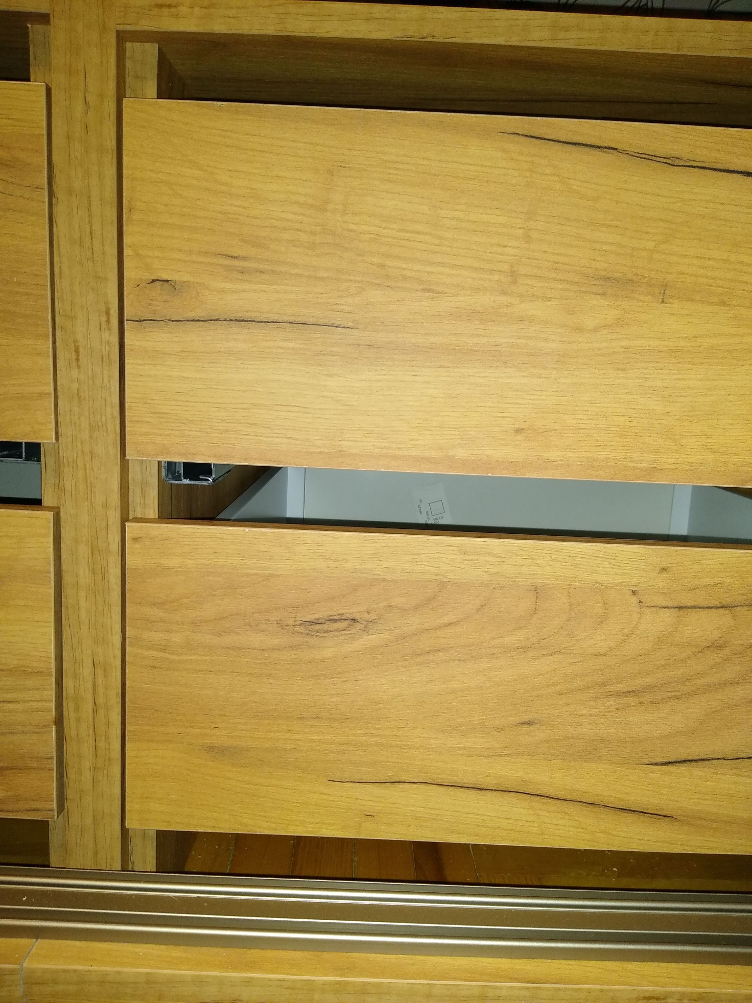 Szczegółowe ujęcie frontów szuflad z drewna o jasnym odcieniu, widoczna struktura słojów i delikatne pęknięcia, metalowe prowadnice szuflad.