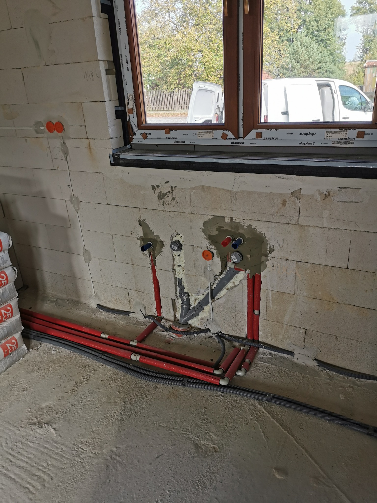 Świeżo wykonane podejścia instalacyjne wodno-kanalizacyjne w ścianie z betonu komórkowego, widoczne rury z tworzywa sztucznego w kolorze czerwonym i szarym, częściowo zamurowane, z widocznymi...