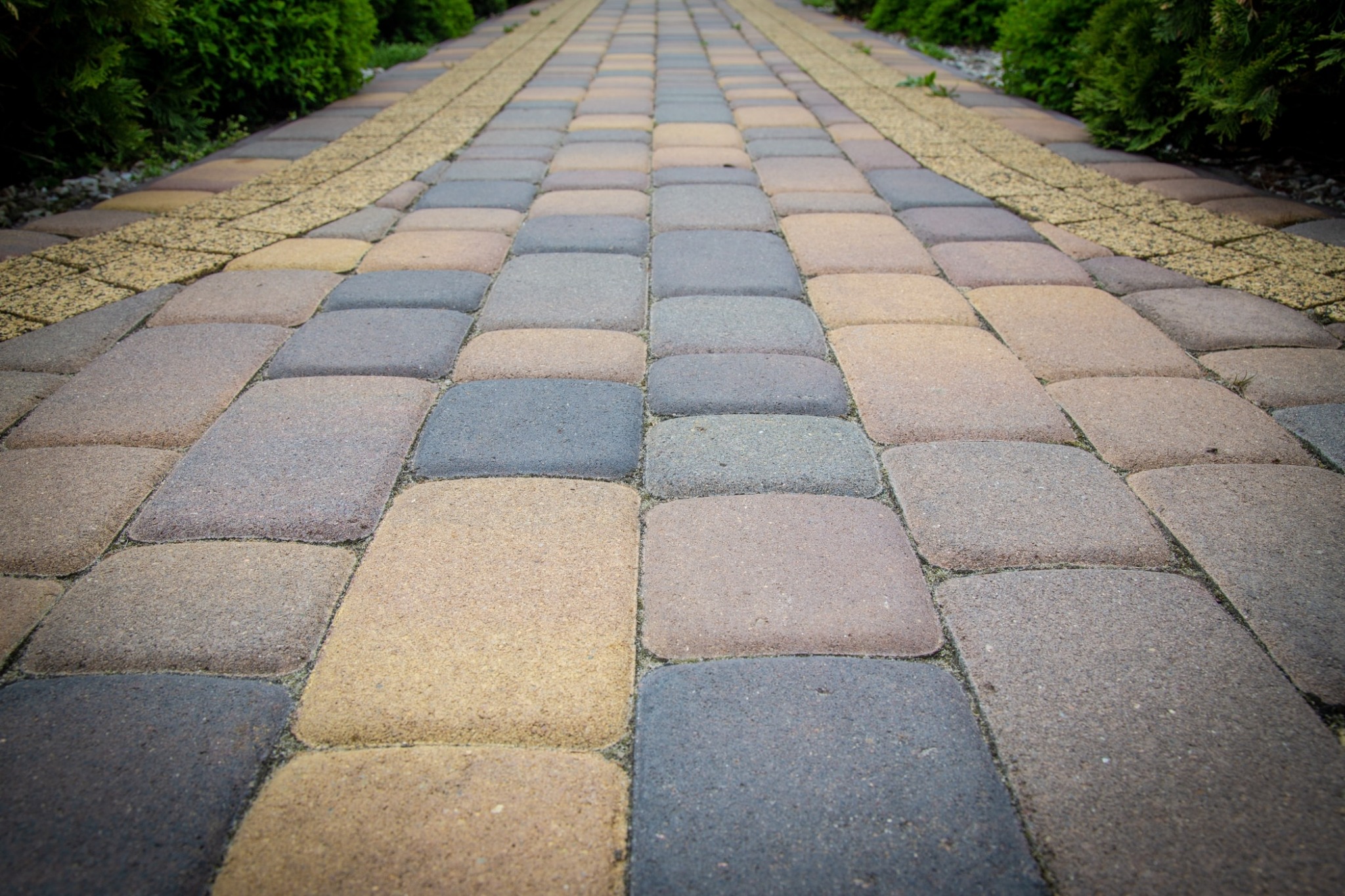 Ułożona kostka brukowa w Przemyślu, z widoczną linią drenażową po bokach i zielonymi krzewami w tle, perspektywa z dołu do góry.