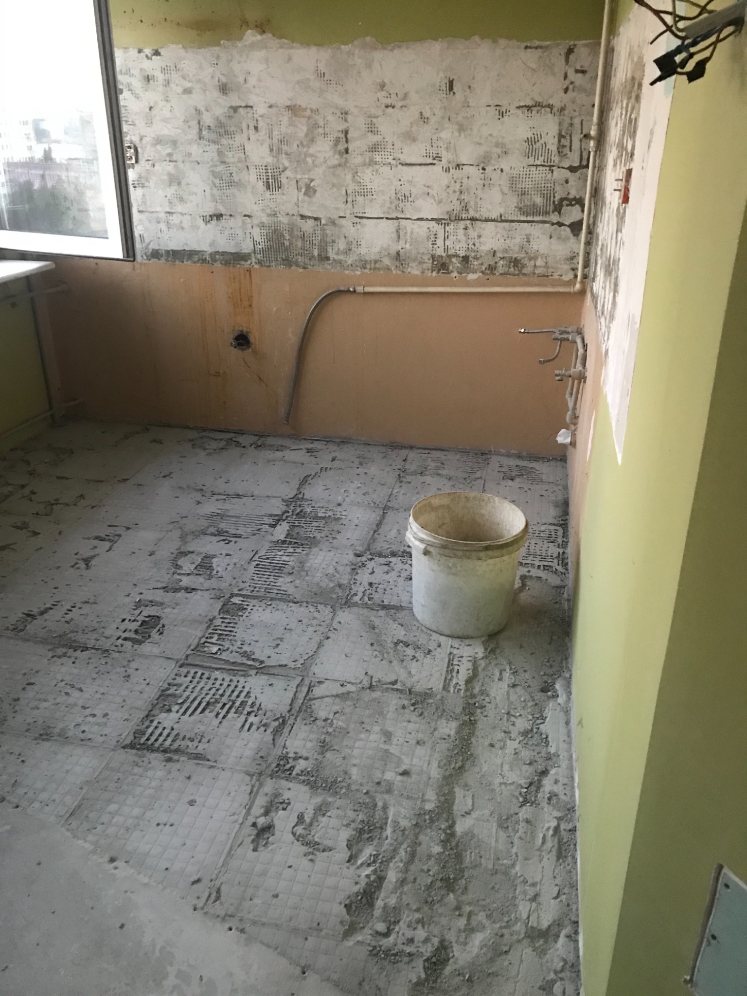 Demontaż starych płytek podłogowych w trakcie remontu łazienki, widoczne fragmenty starej podłogi, ściany przygotowane do położenia płytek i wiadro