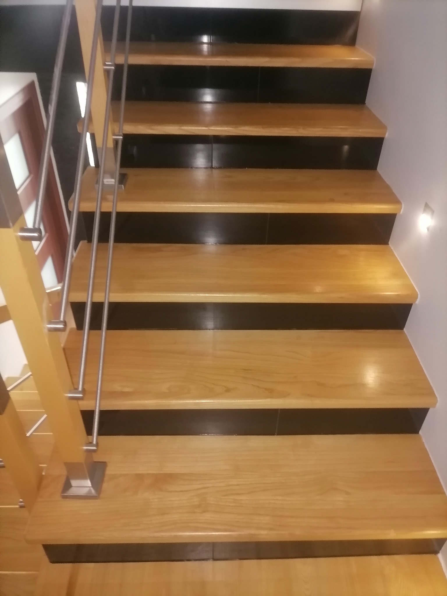 Schody drewniane z czarnymi podstopnicami i metalową balustradą w domu w Rzeszowie, oświetlone punktowym światłem.