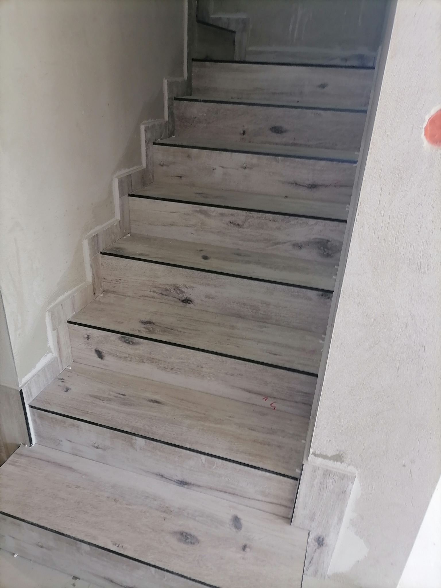 Schody wykończone panelami imitującymi drewno, widoczne niedociągnięcia w wykończeniu ścian.