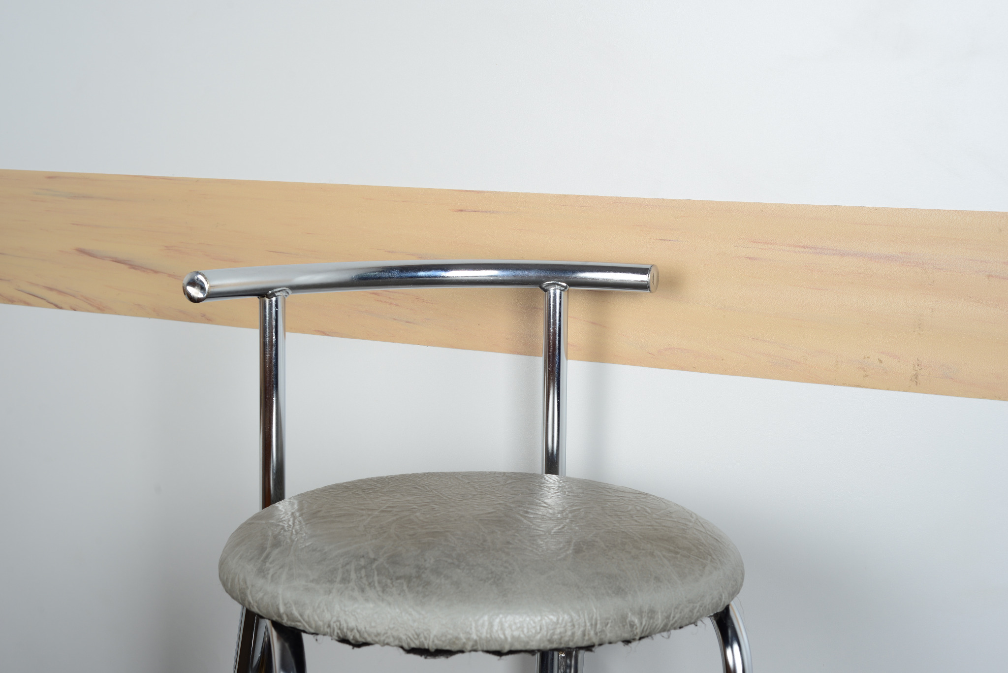 Zbliżenie na odbojnicę ścienną w kolorze jasnego drewna, zamontowaną poziomo na białej ścianie, z fragmentem chromowanego krzesła barowego na pierwszym planie.