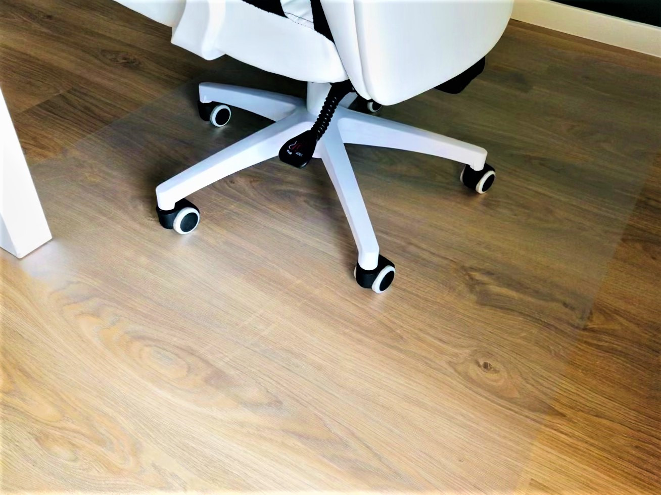 Przezroczysta mata ochronna pod krzesło biurowe na drewnianej podłodze, widoczne kółka białego krzesła i fragment biurka.