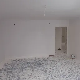 Świeżo pomalowane na biało wnętrze pokoju z zabezpieczoną folią podłogą, widoczna drabina z oświetleniem budowlanym.