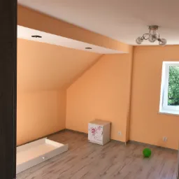 Pomalowane na brzoskwiniowo poddasze pokoju dziecięcego z oknem, białą komodą z motywem księżniczki i zieloną piłką na podłodze z paneli.