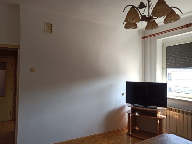 Jasne wnętrze pokoju po remoncie: świeżo pomalowane ściany w odcieniu bieli, parkiet ułożony w jodełkę, widoczny fragment telewizora i mebli.