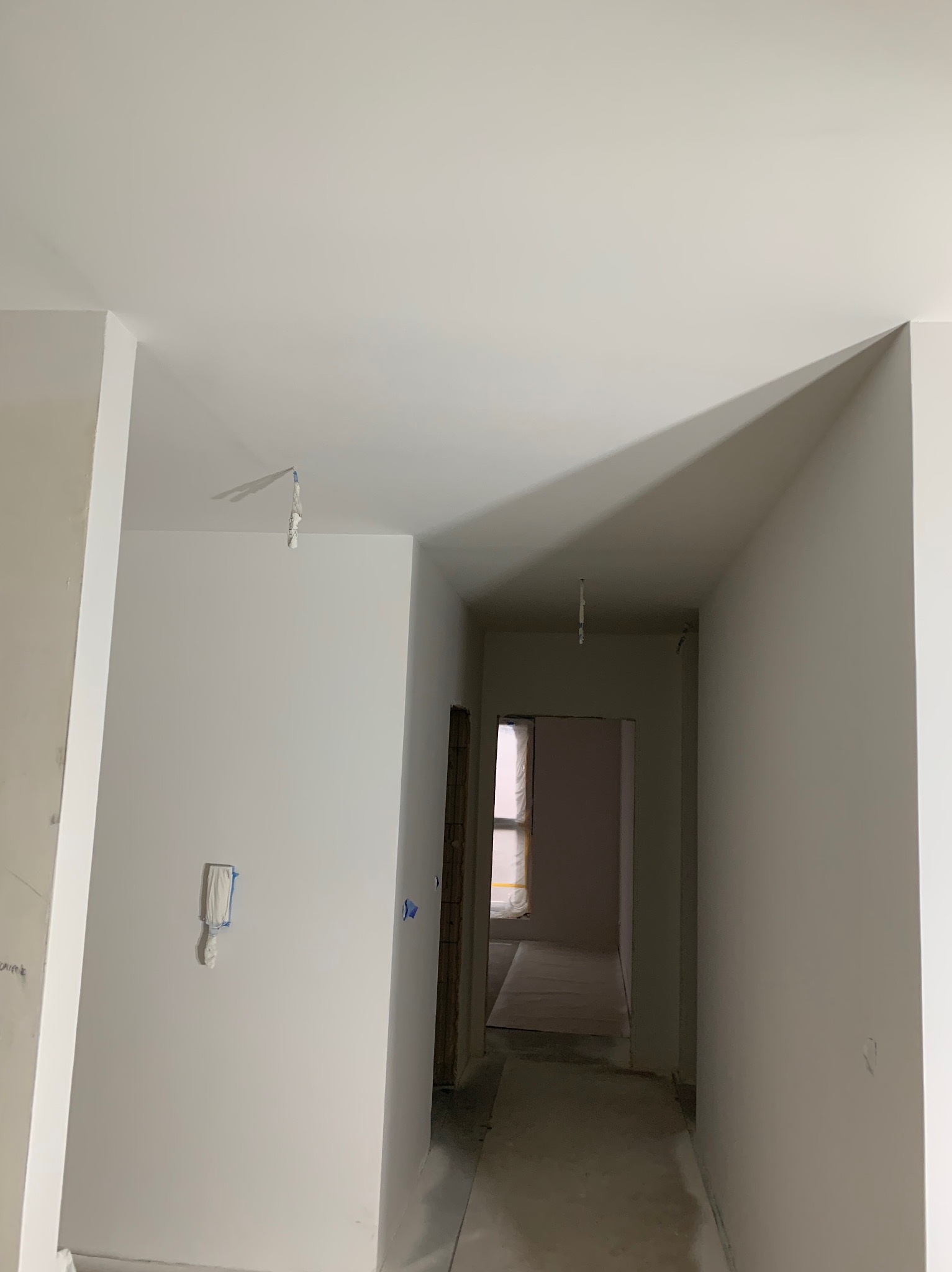 Pomieszczenie w trakcie prac wykończeniowych: świeżo pomalowane na biało ściany i sufit, zabezpieczona folią futryna drzwiowa, widoczne ślady po taśmie malarskiej, na suficie wiszące resztki...