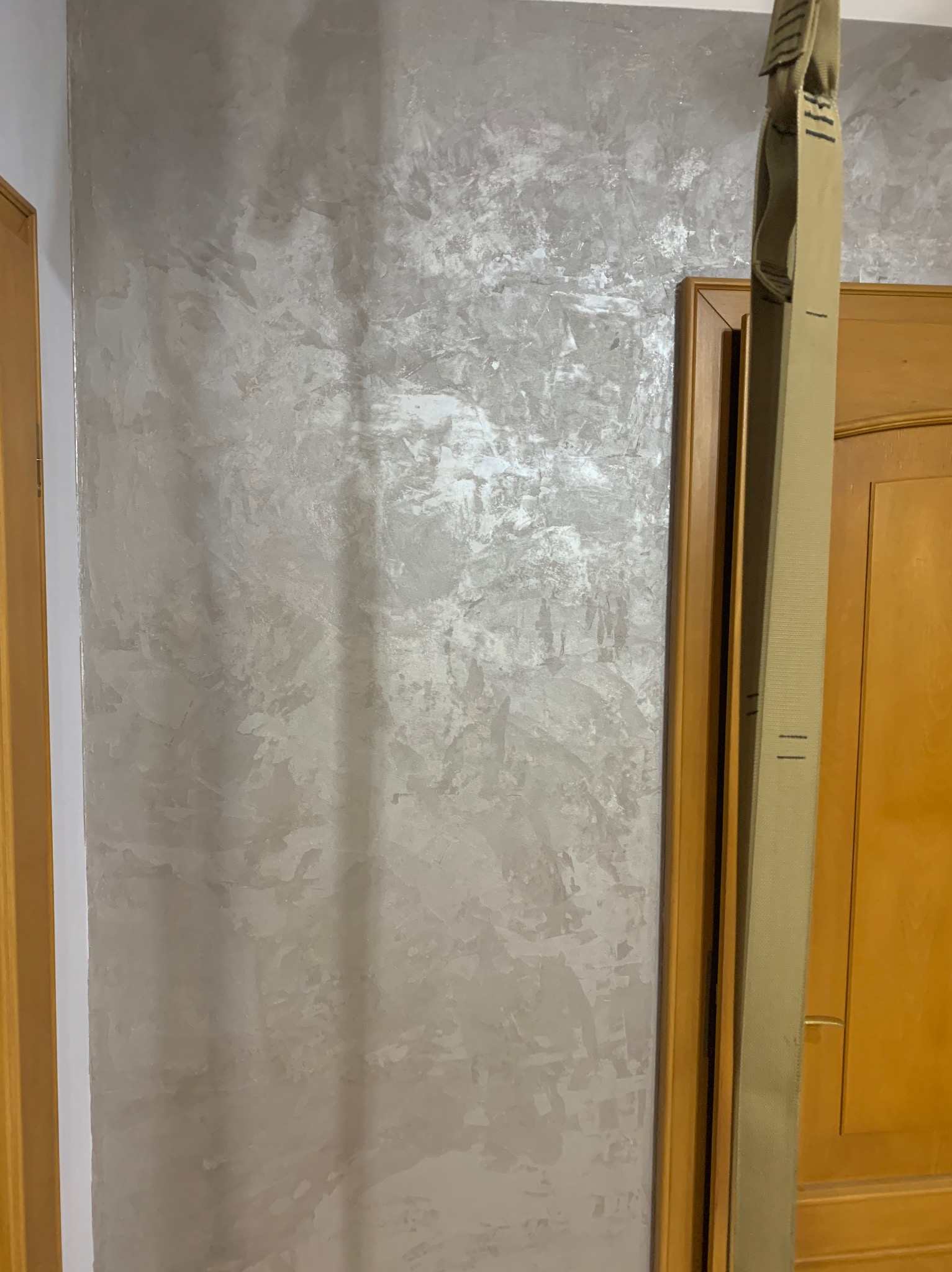 Ściana z efektem dekoracyjnym w odcieniach szarości, widoczna obok ościeżnicy i fragmentu drzwi z drewna.