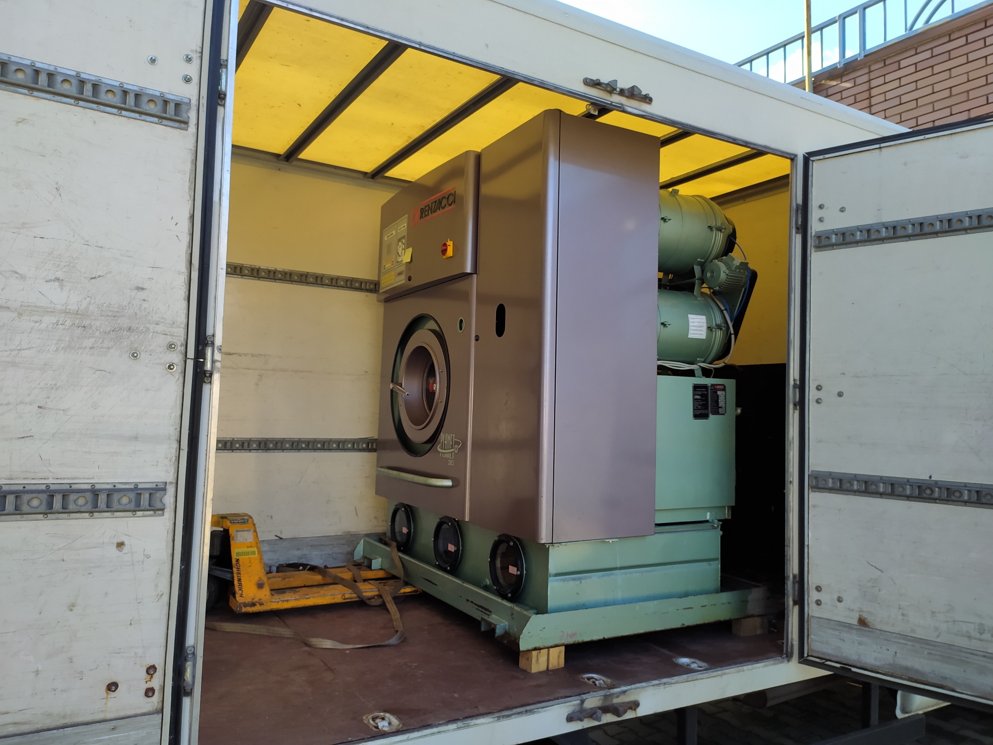 Duża przemysłowa pralnico-wirówka marki Renzacci Planet 30, zabezpieczona wewnątrz skrzyni transportowej busa, widoczny wózek paletowy.