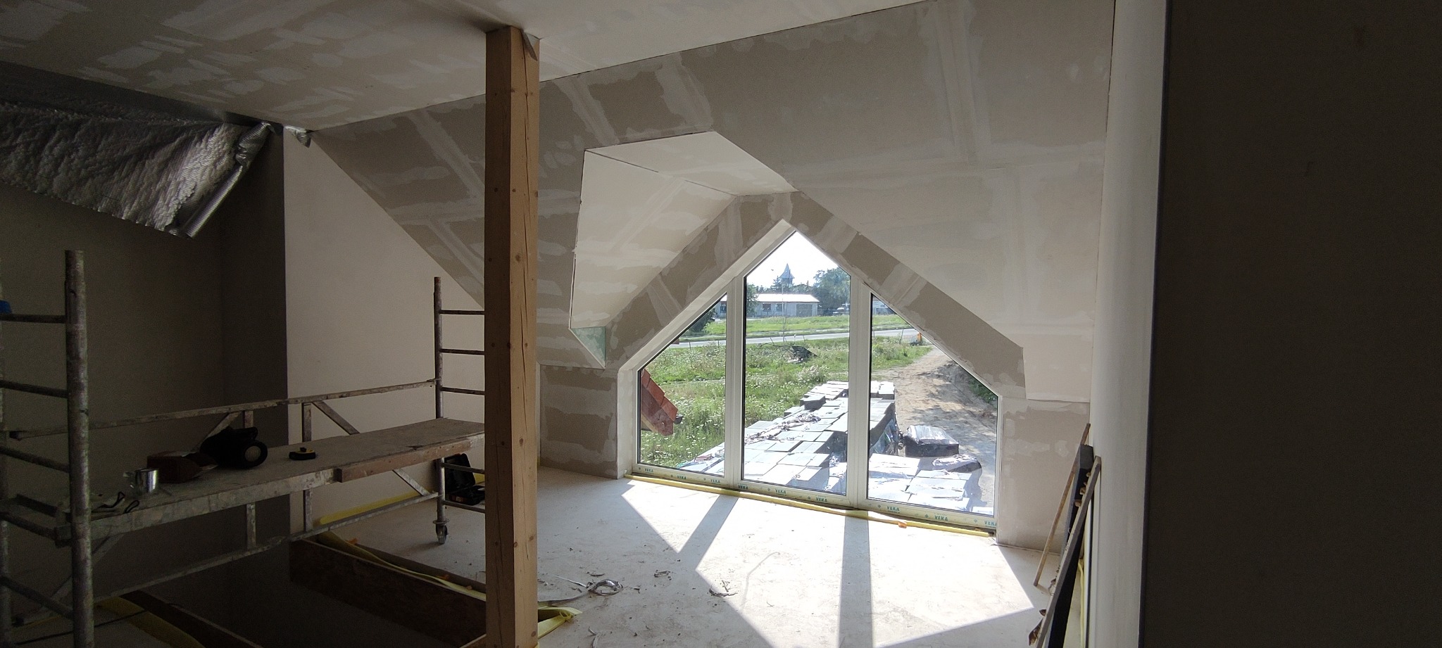 Montaż płyt karton gips na poddaszu w Lubinie, widoczna drewniana belka konstrukcyjna i okno dachowe z widokiem na zewnątrz.