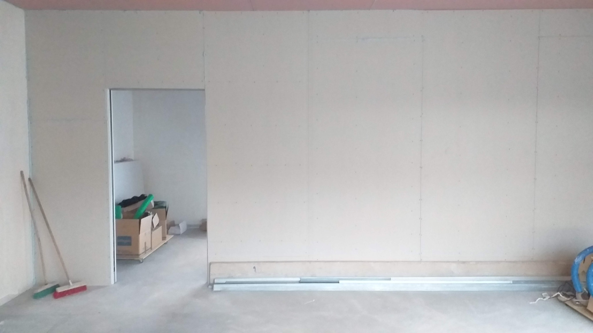 Wnętrze w trakcie montażu ścian działowych z płyt gipsowo-kartonowych, widoczne profile metalowe na podłodze, szpachlowane łączenia płyt oraz narzędzia w tle.
