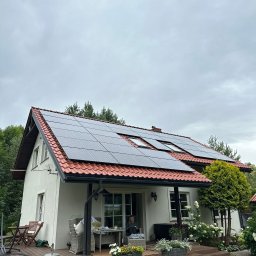 Metis Intech Sp. z o.o. - Dom jednorodzinny z czerwoną dachówką i panelami fotowoltaicznymi na dachu, widok z ogrodu w pochmurny dzień.