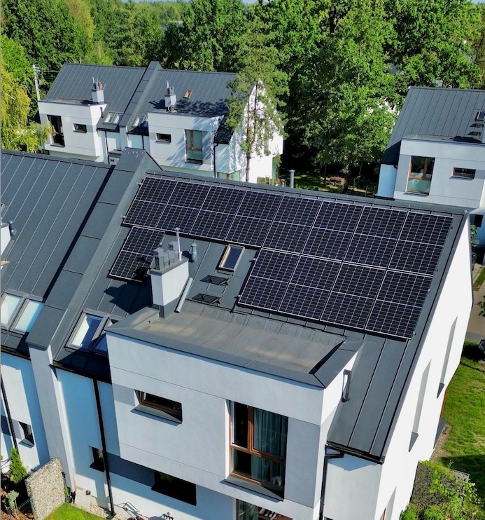 Instalacja paneli słonecznych na dachu szeregowca z szarej blachy, widok z góry, słoneczny dzień.