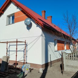 Dapir sp zoo - Świeżo otynkowany dom jednorodzinny z czerwoną dachówką i detalami w kolorze pomarańczowym, widoczne rusztowania i elementy przygotowane do dalszych prac wykończeniowych.