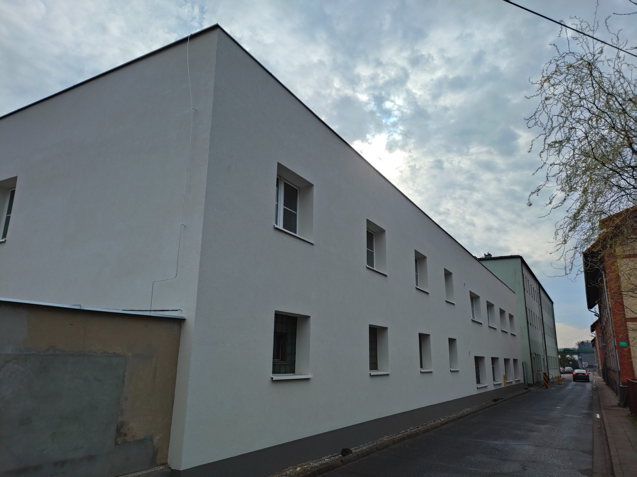 Odnowiony budynek z nową, jasną elewacją i prostokątnymi oknami, widok z ulicy w pochmurny dzień.