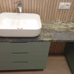 Nowoczesna łazienka: biała, kwadratowa umywalka na zielonym blacie z granitu, zamontowana na szafce z trzema szufladami w pastelowym odcieniu zieleni, drewniana boazeria na ścianie.