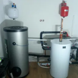 Dwa zbiorniki akumulacyjne: srebrny z logo GOE i biały, połączone rurami, z widocznymi elementami instalacji, narzędzia w skrzynce po lewej stronie, instalacja w surowym stanie.