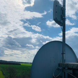 Instal-SAT Damian Moskal - Antena satelitarna i dodatkowa instalacja na dachu budynku we Wrocławiu, z widokiem na pola i zachmurzone niebo.