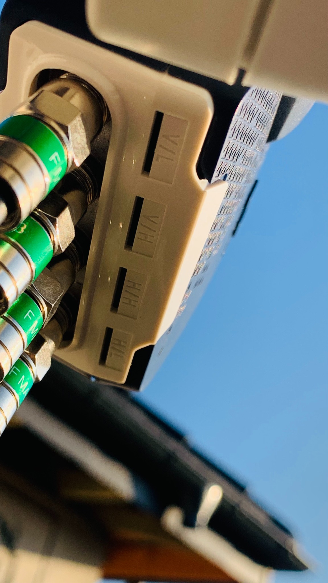 Złącza antenowe F-MA z zielonymi pierścieniami, podłączone do białego rozdzielacza antenowego na tle błękitnego nieba.