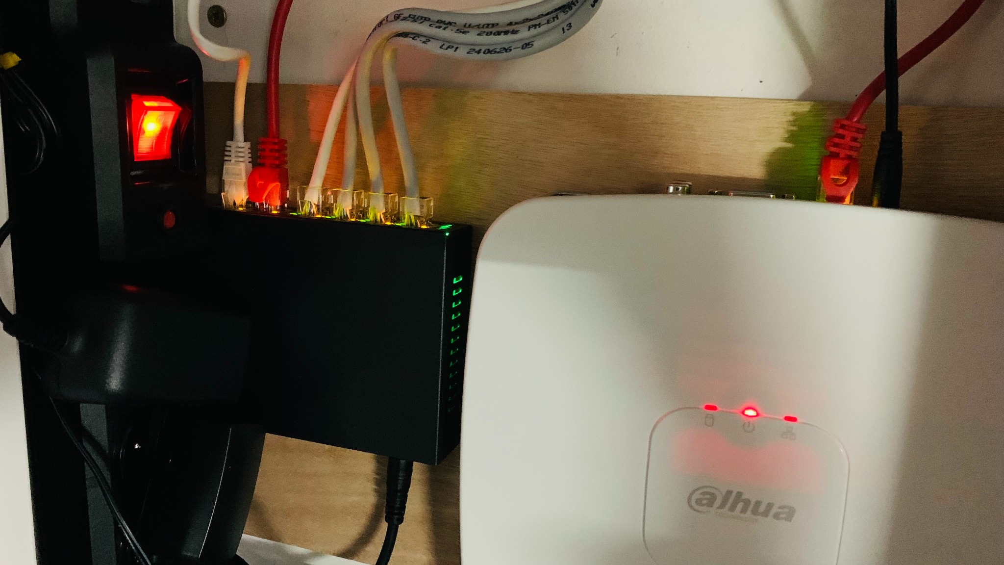 Czarny switch sieciowy z podłączonymi kablami Ethernet, obok biały punkt dostępowy Dahua z diodami sygnalizacyjnymi, zamontowane na drewnianej płycie.