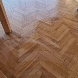 Ułożony parkiet w jodełkę z widocznym fragmentem okna i drewnianej ściany w jasnym, nowoczesnym wnętrzu, z widocznymi smugami po czyszczeniu.