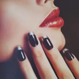 Zbliżenie na kobiecą twarz z intensywnie czerwoną szminką i dłonią z czarnymi paznokciami z srebrnymi końcówkami, prezentujące elegancki manicure.