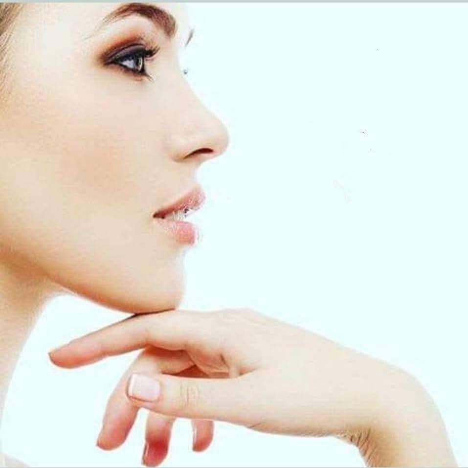 Profil kobiety z delikatnym makijażem oczu i naturalnym manicure na tle jasnoniebieskim, dłoń podpierająca podbródek.