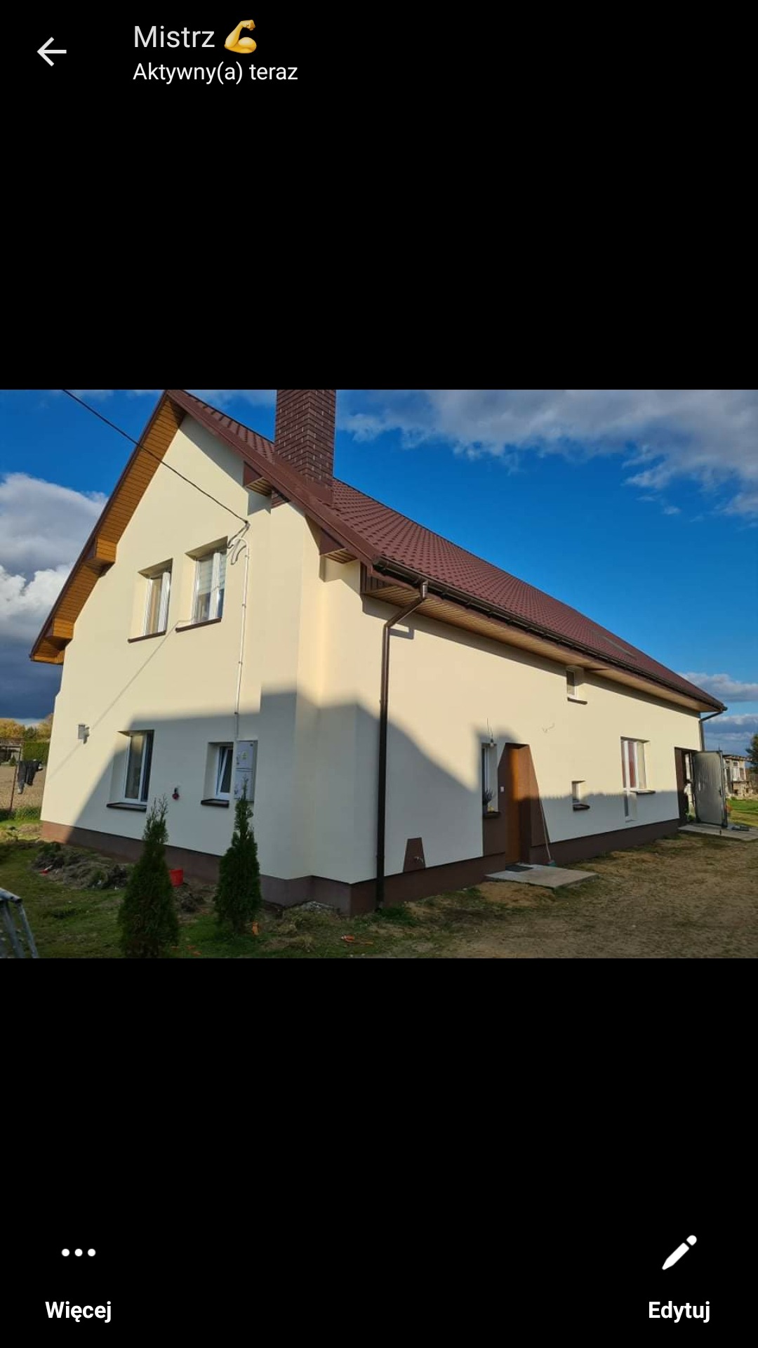 Ocieplony dom jednorodzinny z beżową elewacją, brązowym dachem i podbitką, widoczne okna i drzwi, na trawniku małe drzewka iglaste.