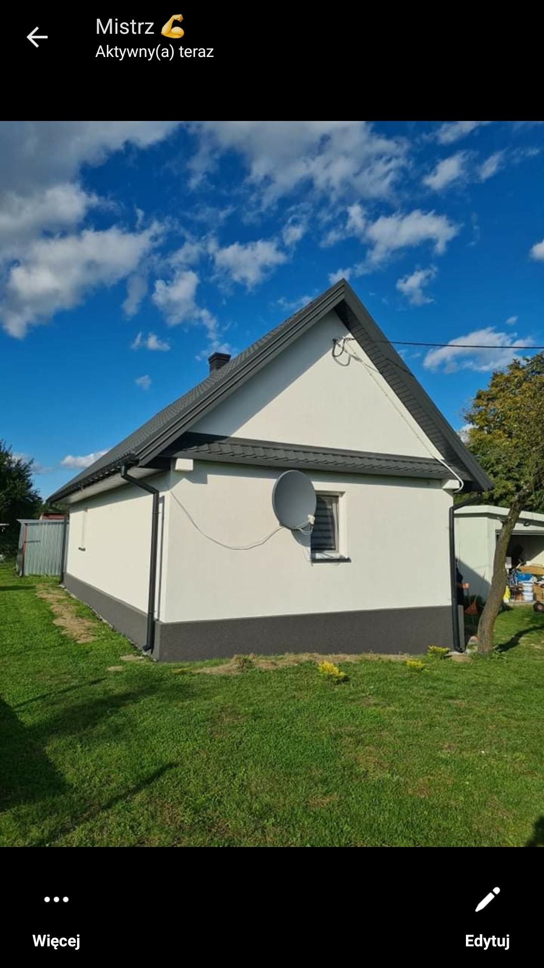 Jednopiętrowy dom z białą elewacją i szarą podmurówką, szary dach, antena satelitarna na ścianie, widok z trawnika w słoneczny dzień.