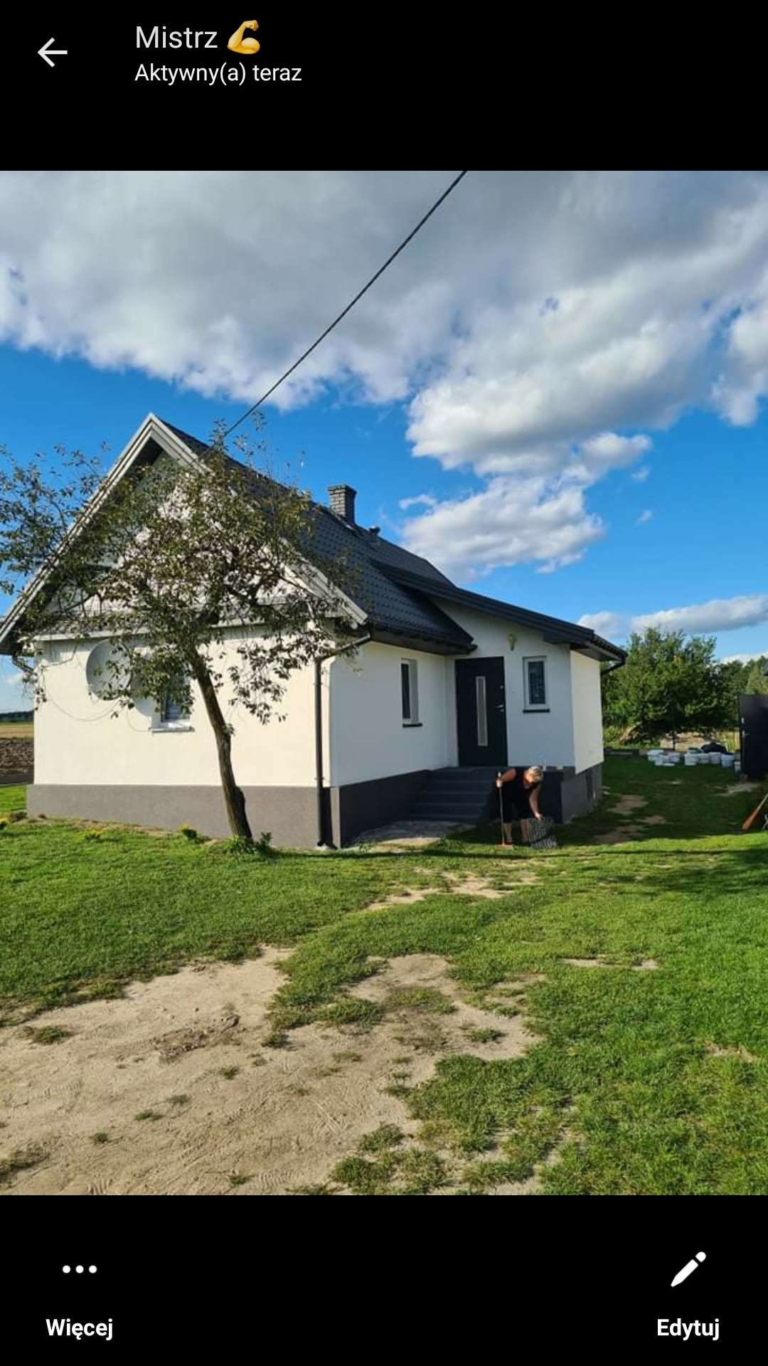 Dom jednorodzinny z białą elewacją i szarym cokołem, czarnym dachem i drzewem na pierwszym planie, widoczna osoba przy wejściu.