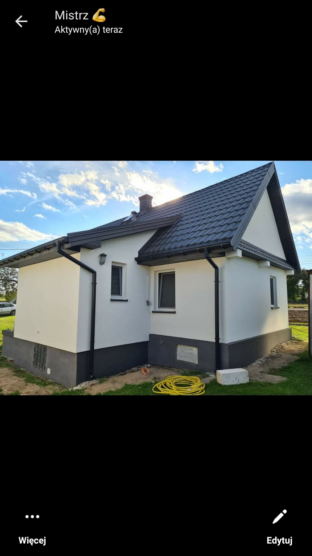 Dom jednorodzinny po renowacji elewacji, z jasną fasadą i ciemną podmurówką oraz dachem, widoczne rury spustowe i zwinięty wąż ogrodowy na trawniku.