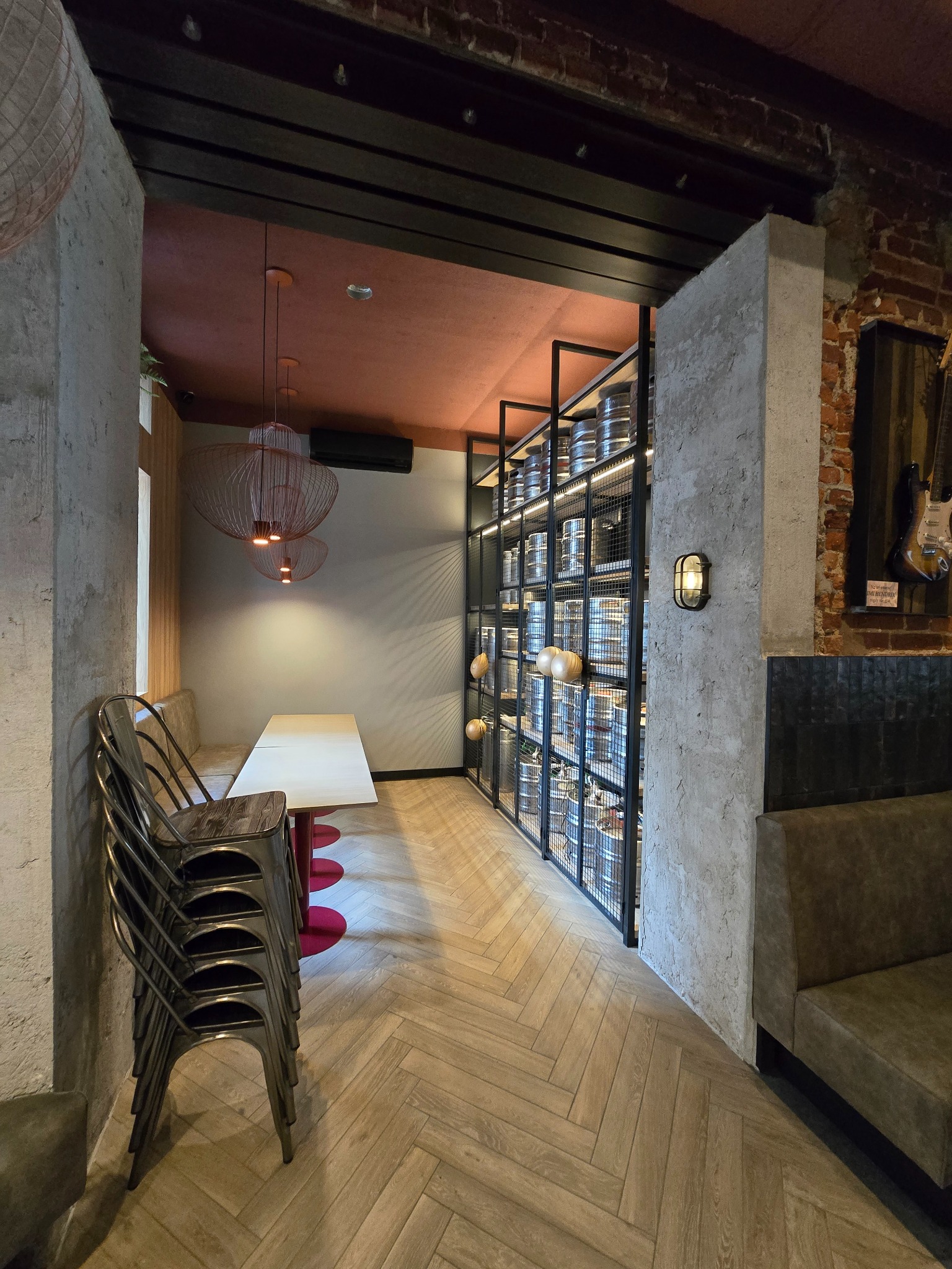 Loftowe wnętrze restauracji: surowe ściany, drewniana podłoga w jodełkę, metalowa regał z beczkami, designerskie lampy i stos krzeseł.