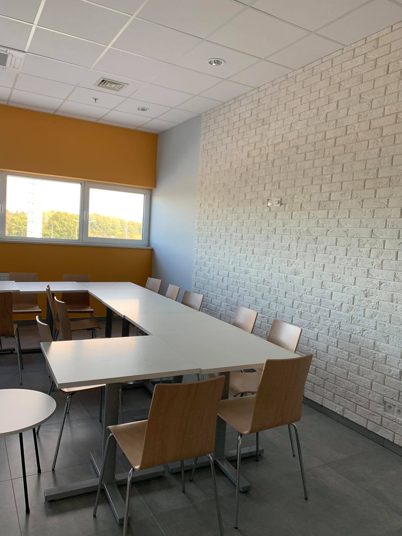 Jasne biuro z długim białym stołem konferencyjnym, krzesłami z jasnego drewna i ścianą wykończoną białą cegłą dekoracyjną.
