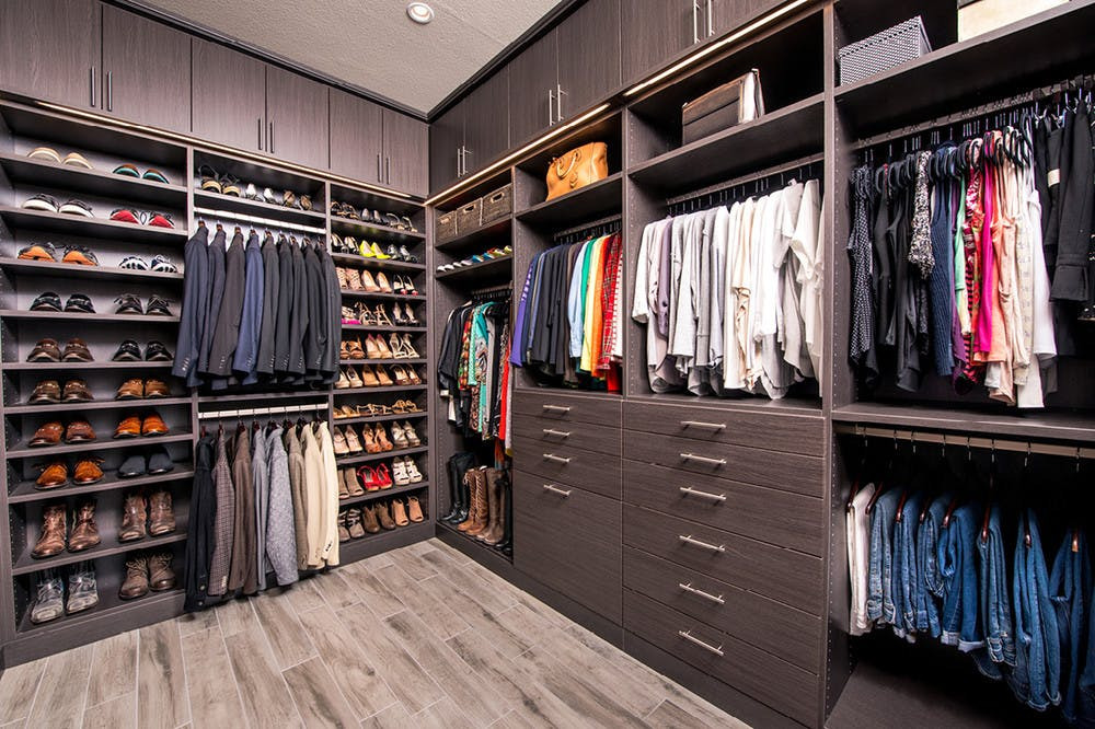 Przestronna garderoba na wymiar z ciemnego drewna, z półkami na buty, wieszakami na ubrania i szufladami, oświetlona punktowo, z podłogą imitującą drewno.