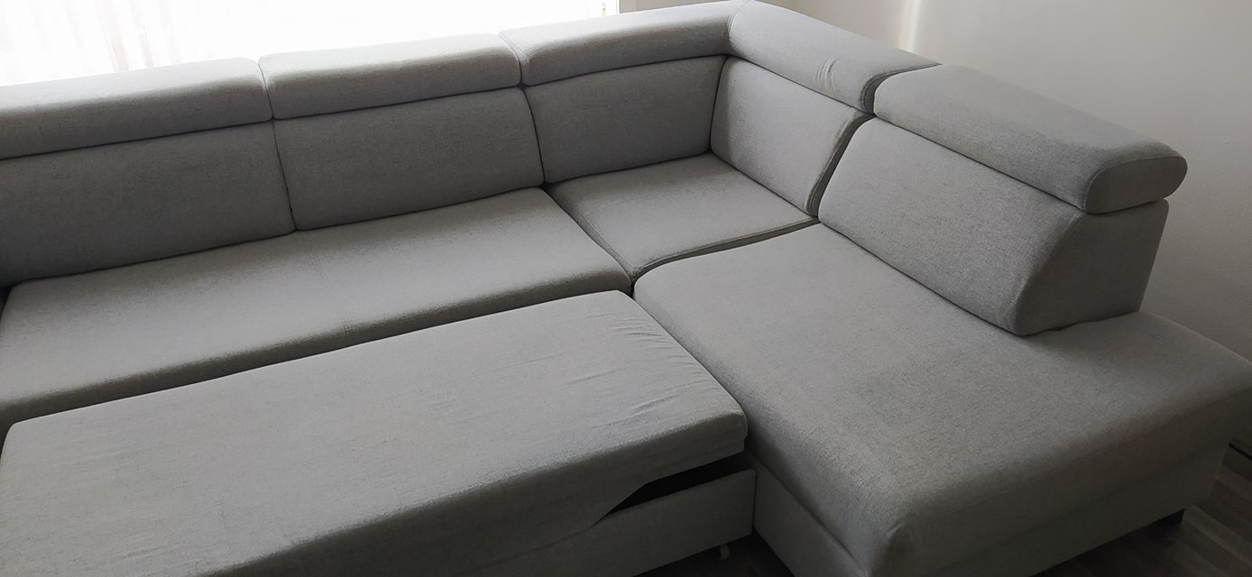 Szary narożnik z funkcją spania, widoczny otwarty schowek na pościel, minimalistyczny design.