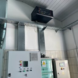 AURUM IT sp. z o.o. - Szafa rack na suficie z korytkami kablowymi, obok tablice rozdzielcze z przyciskami i wskaźnikami. Instalacja w pomieszczeniu technicznym.